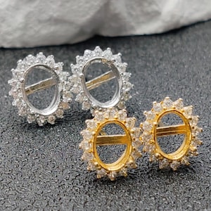 Op de afbeelding: Close-up van vier ovale oorbelzettingen. Twee zijn zilverkleurig en twee goudkleurig. Elke zetting is omgeven door kleine, heldere edelstenen, waardoor een halo-effect ontstaat. De oorbellen worden gepresenteerd op een donkergrijze ondergrond.