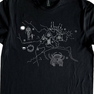May include: Black t-shirt with a white graphic depicting ancient petroglyphs. The design includes human figures, circles, and abstract shapes, offering a unique artistic aesthetic. Ideal for those with an interest in history and art.