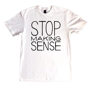 Könnte beinhalten: Weißes T-Shirt mit dem schwarzen Aufdruck "STOP MAKING SENSE". Der Text ist in drei Zeilen angeordnet. Das T-Shirt hat einen Rundhalsausschnitt und kurze Ärmel. Die Schriftart ist fett und serifenlos.