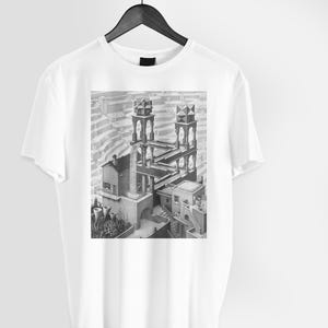 Può includere: Maglietta bianca con un'illustrazione in bianco e nero di un edificio con un'architettura impossibile. L'illustrazione è una classica illusione ottica.