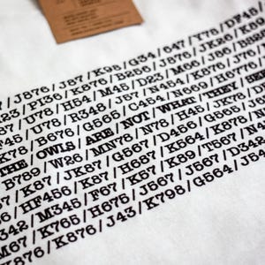 May include: A white t-shirt with black text that reads "THE OWLS ARE NOT WHAT THEY SEEM" and a series of letters and numbers.