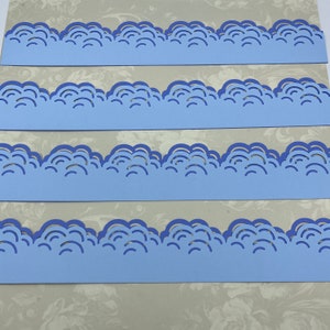 May include: Four strips of light blue paper with a scalloped edge design. The scalloped edge is a repeating pattern of rounded shapes.