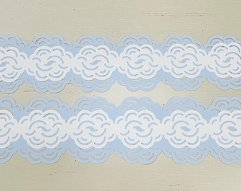 May include: Two decorative paper borders with a cloud design. Each border has a light blue base with white cloud cutouts. The cloud shapes are layered, creating a three-dimensional effect. The borders are ideal for scrapbooking or crafting.