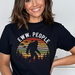 May include: Black t-shirt with a retro sunset graphic featuring a Bigfoot silhouette and the text "EWW, PEOPLE".