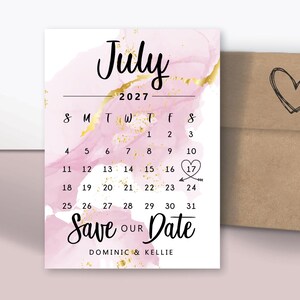 May include: Custom magnets featuring a July 2027 calendar with a highlighted date. The design includes pink watercolor and gold accents, with the text "Save Our Date." An envelope with a heart is also included.