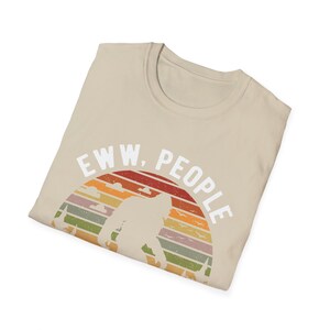 May include: A beige t-shirt with a retro sunset graphic and the text "EWW, PEOPLE" in white. The graphic features a silhouette of a Bigfoot walking across the sunset.