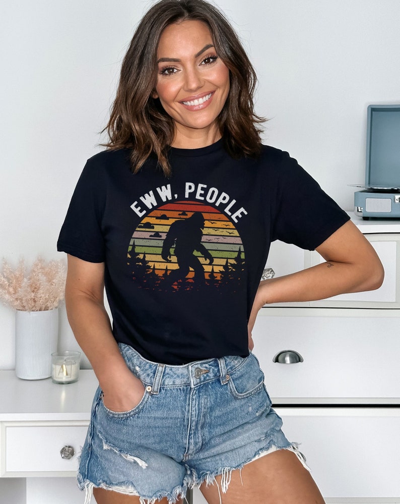 May include: Black t-shirt with a retro sunset graphic featuring a Bigfoot silhouette and the text "EWW, PEOPLE".
