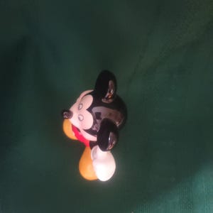 Puede incluir: Una figura de cer&aacute;mica de Mickey Mouse, con cabeza y orejas negras, cara blanca y atuendo rojo y amarillo. La figura es brillante y tiene un dise&ntilde;o de dibujos animados cl&aacute;sico.