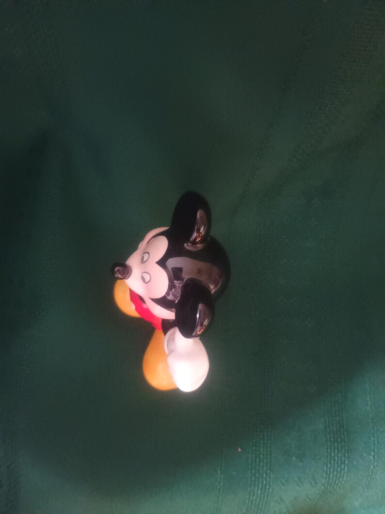 Puede incluir: Una figura de cer&aacute;mica de Mickey Mouse, con cabeza y orejas negras, cara blanca y atuendo rojo y amarillo. La figura es brillante y tiene un dise&ntilde;o de dibujos animados cl&aacute;sico.