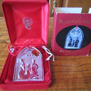 May include: A Waterford Crystal Christmas ornament in a red box. The ornament is a clear glass depiction of the Nativity scene with the text "1995" on the bottom. The box has the text "Waterford Crystal" on the front.