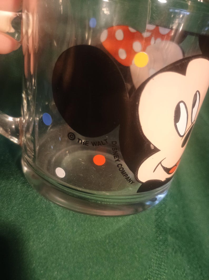 Pu&ograve; includere: Tazza di vetro trasparente con un disegno a cartoni animati di Minnie Mouse. La tazza ha un manico ed &egrave; decorata con pois e la scritta "THE WALT DISNEY COMPANY". Il vetro trasparente permette di vedere il contenuto.