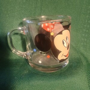 Pu&ograve; includere: Tazza di vetro trasparente con Topolino. La tazza ha un manico e un design colorato del volto di Topolino e pois. Le parole "The Walt Disney Company" sono stampate sulla tazza.