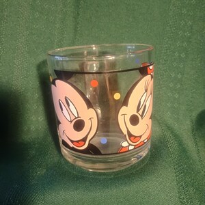 Pu&ograve; includere: Bicchiere di vetro trasparente con i personaggi dei cartoni animati di Topolino e Minnie. Il bicchiere ha un bordo nero e pois colorati. I personaggi dei cartoni animati sono rosa, neri, rossi e bianchi.