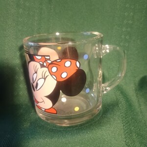 Pu&ograve; includere: Tazza di vetro trasparente con un'immagine a cartoni animati di Minnie Mouse. Il design include il volto di Minnie, un fiocco rosso a pois bianchi e pois colorati. La tazza ha un manico ed &egrave; adatta alle bevande.