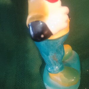 May include: A vintage figurine of a cartoon character, featuring a red bow tie, yellow shirt, and blue pants. The figurine has a white face and black ears. The base and shoes are light blue and yellow.