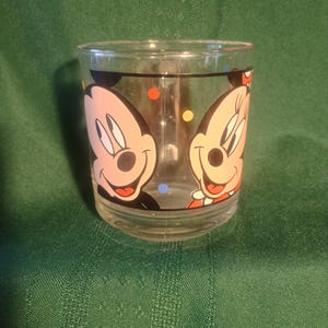 Pu&ograve; includere: Bicchiere di vetro trasparente con i personaggi dei cartoni animati di Topolino e Minni. Il bicchiere ha una forma arrotondata ed &egrave; decorato con pois colorati. I personaggi sorridono.