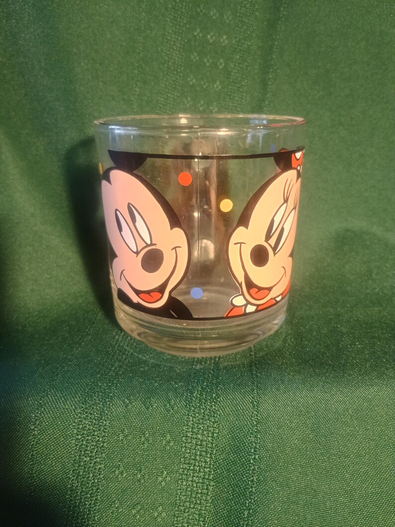 Pu&ograve; includere: Bicchiere di vetro trasparente con i personaggi dei cartoni animati di Topolino e Minni. Il bicchiere ha una forma arrotondata ed &egrave; decorato con pois colorati. I personaggi sorridono.