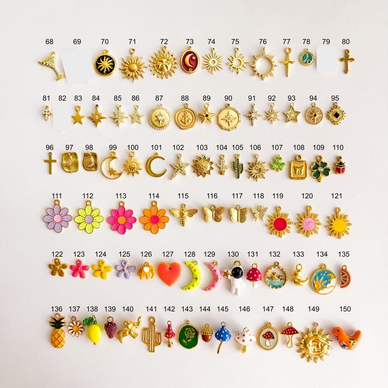 May include: A collection of gold-tone and colorful enamel charms arranged in rows, each labeled with numbers 68 through 150. The charms feature various shapes including suns, stars, flowers, animals, celestial symbols, and food items on a white background.