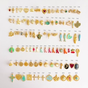 May include: A collection of assorted metal charms arranged in rows, each labeled with a unique identification number from 714 to 802. The charms feature various shapes including hearts, animals, keys, crosses, and floral motifs in gold tones.