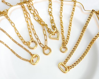 May include: A collection of gold-colored necklaces with various chain styles and pendant designs. The necklaces include a heart-shaped pendant, circular rings, and a clasp closure. The jewelry is displayed on a white, scalloped-edge plate.