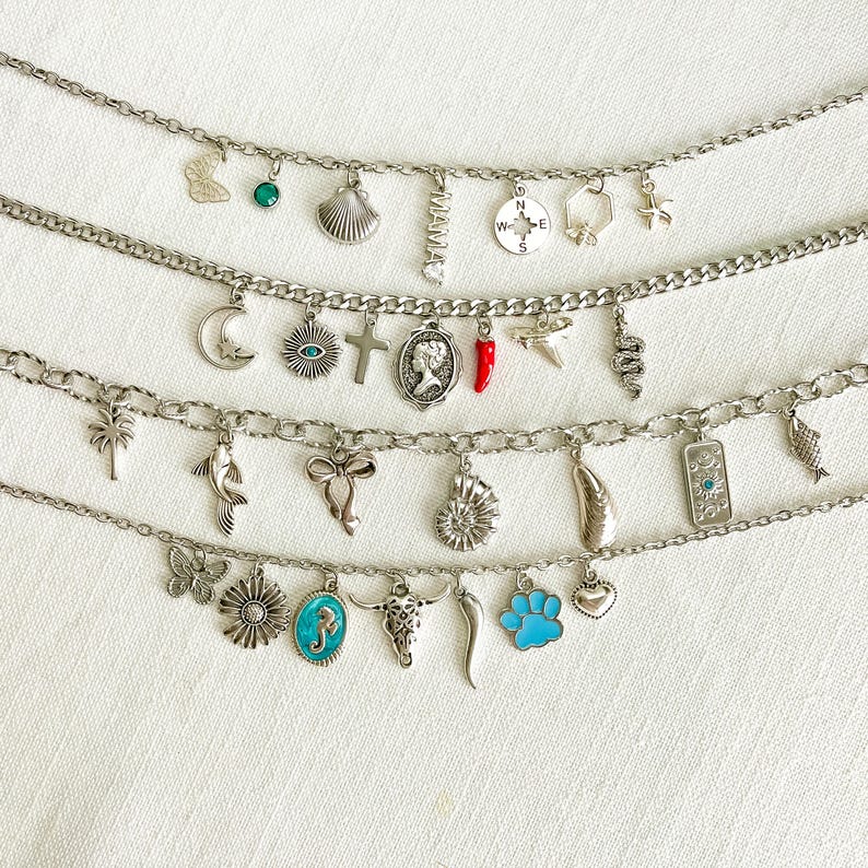 May include: Four silver-toned charm bracelets featuring various pendants including a butterfly, seashell, compass, moon, cross, cameo, red chili pepper, snake, palm tree, fish, bow, ammonite, cow skull, blue paw print, and the word MAMA.