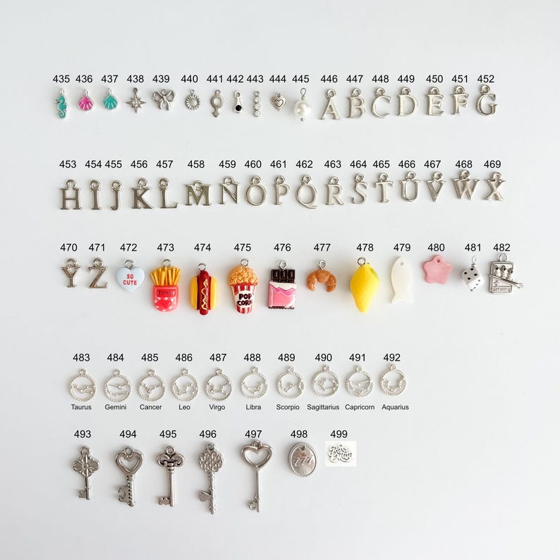 May include: A collection of metal and enamel charms arranged in rows, numbered 435 through 499. The set includes alphabet letters, food items like popcorn and fries, zodiac symbols, keys, and various shapes, each with a small loop for attachment.