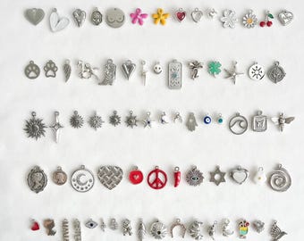 May include: A collection of assorted metal charms arranged in five horizontal rows. The charms feature various shapes including hearts, flowers, animals, celestial symbols, geometric patterns, and food items in silver, gold, and colored enamel finishes.