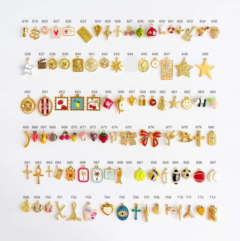 May include: A collection of small metal charms arranged in rows, each labeled with a number from 618 to 713. The charms feature various shapes including hearts, stars, fruits, sports equipment, and symbols, finished in gold-tone metal and enamel.
