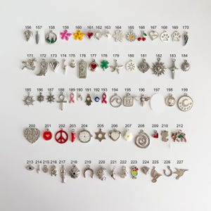 May include: A collection of metal charms arranged in rows and numbered from 156 to 227. The charms feature various shapes including hearts, flowers, animals, symbols, and food items, with some incorporating colored enamel accents.