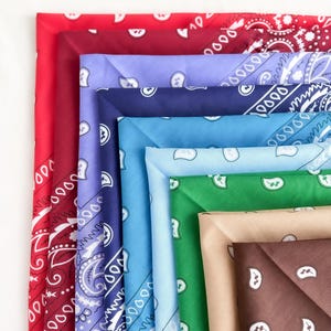 May include: A collection of square fabric bandanas featuring a traditional paisley pattern in various colors including red, burgundy, lavender, navy blue, light blue, bright green, tan, and dark brown, all neatly stacked and layered in a row.