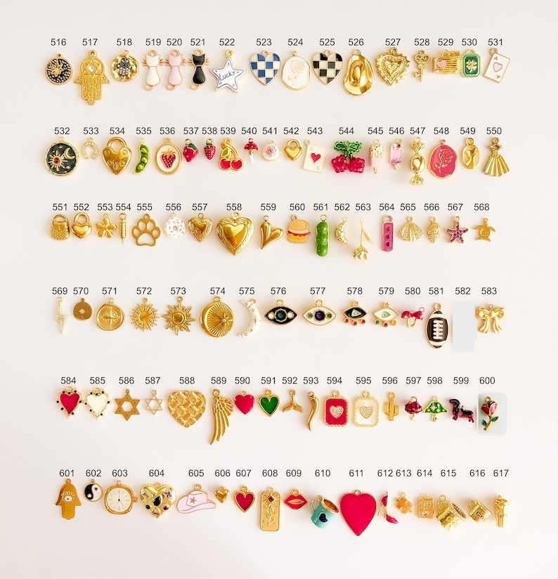 May include: A collection of small metal charms arranged in rows, each labeled with a number from 516 to 617. The charms feature various shapes including hearts, stars, animals, food items, symbols, and objects, finished in gold tones with enamel.