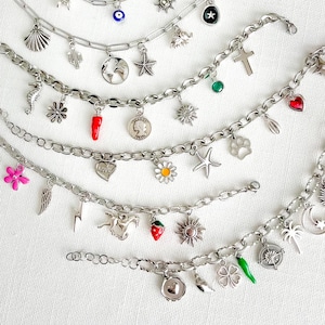 May include: A collection of silver-toned charm bracelets featuring various metal pendants including a seashell, cactus, globe, starfish, seahorse, flower, chili pepper, coin, cross, heart, paw print, lightning bolt, horse, strawberry, sun, and compass.