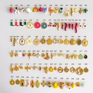 May include: A collection of small metal and enamel charms arranged in rows, numbered 151 through 240. The charms feature various shapes including animals, flowers, food items, symbols, and geometric designs in gold, silver, and vibrant colors.