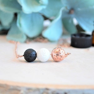 May include: A rose gold chain necklace with three lava stone beads. The beads are black, white, and rose gold.