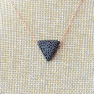 May include: A rose gold chain necklace with a black triangle pendant made of lava rock.