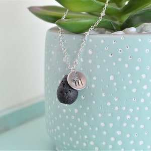 May include: A silver chain necklace with a black lava rock pendant and a silver charm with the letter "M" engraved on it.