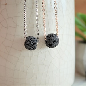 Puede incluir: Dos collares difusores de piedra de lava, uno con una cadena plateada y otro con una cadena de oro rosa. Las piedras de lava son negras y redondas.