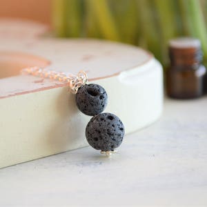 May include: A silver chain necklace with two black lava rock beads. The necklace is on a white surface.