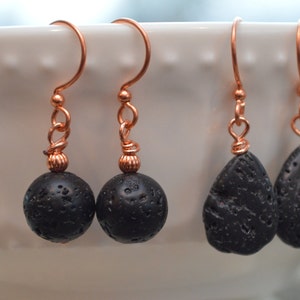 May include: Three pairs of earrings with black lava rock beads and copper wire hooks. The earrings are displayed on a white ceramic bowl.