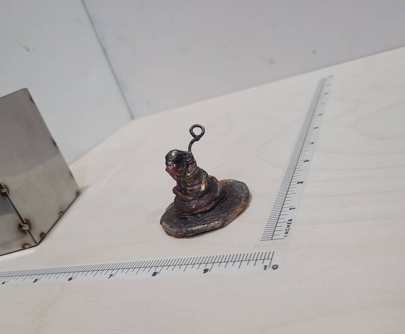Peut inclure: Une petite sculpture d&eacute;taill&eacute;e en cuivre d'un chapeau de sorcier avec un bord retrouss&eacute; et une boucle de fil sur le dessus.