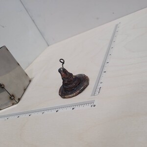 Peut inclure: Un petit chapeau de sorcier en c&eacute;ramique brun avec une boucle de fil sur le dessus. Le chapeau est pos&eacute; sur une surface blanche.
