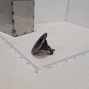 Peut inclure: Une petite sculpture en m&eacute;tal torsad&eacute;e avec une base large et plate et un sommet pointu. La sculpture est de couleur brun fonc&eacute; et semble &ecirc;tre en cuivre.