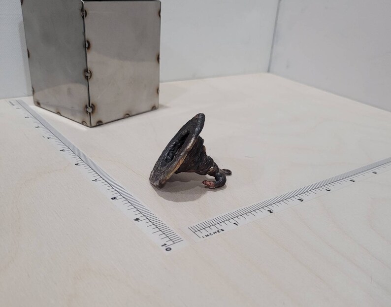 Peut inclure: Une petite sculpture en m&eacute;tal torsad&eacute;e avec une base large et plate et un sommet pointu. La sculpture est de couleur brun fonc&eacute; et semble &ecirc;tre en cuivre.