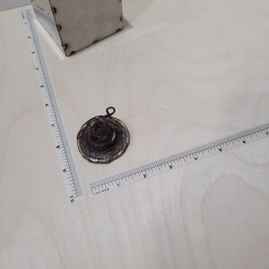 Peut inclure: Un petit pendentif rond et multi-couches en m&eacute;tal avec une patine brune, orange et verte. Le pendentif a une boucle en haut pour l'attacher &agrave; une cha&icirc;ne.