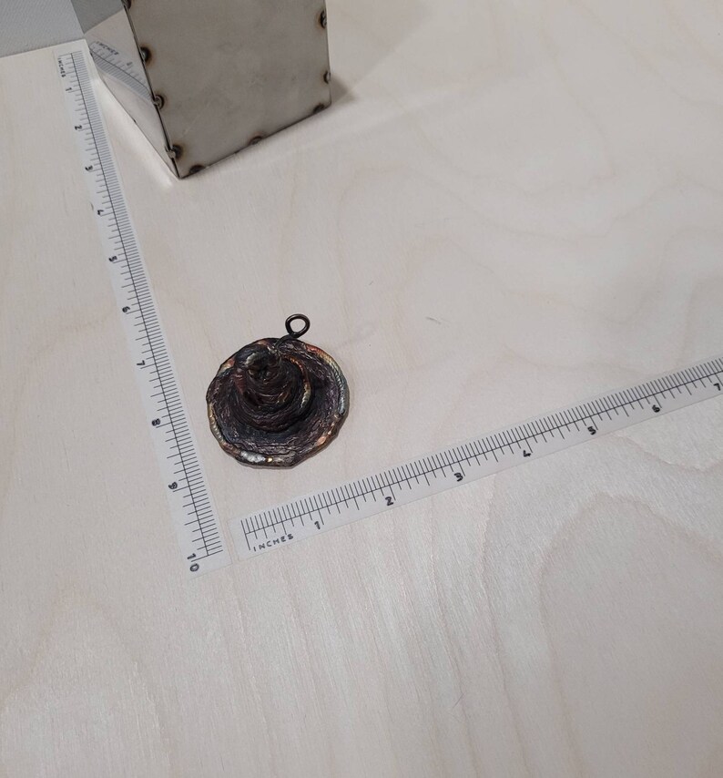 Peut inclure: Un petit pendentif rond et multi-couches en m&eacute;tal avec une patine brune, orange et verte. Le pendentif a une boucle en haut pour l'attacher &agrave; une cha&icirc;ne.