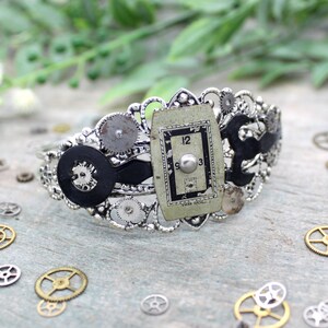 Peut inclure: Un bracelet de style steampunk argenté avec un cadran d'horloge noir et des engrenages. Le bracelet est en métal et présente un design délicat. Le cadran de l'horloge est entouré d'engrenages et d'autres embellissements métalliques.