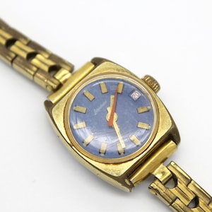 Close up of the dial of a vintage 1970 gold tone Latendresse womens wind up watch. This stylish watch has a blue dial with golden markers and a contrasting vibrant orange hand. It also showcase a date display. The watch informations are written white