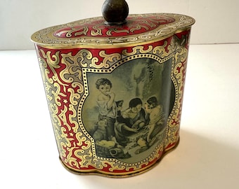 May include: Vintage tin container with a red and gold ornate design. The container features a lid with a dark brown knob and a central image of children. The sides have a repeating pattern of red and gold swirls.