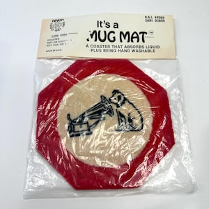 May include: A red, octagonal mug mat with a beige central circle, featuring a black and white illustration of a dog and a gramophone. The packaging reads "It's a MUG MAT" and "A COASTER THAT ABSORBS LIQUID PLUS BEING HAND WASHABLE."