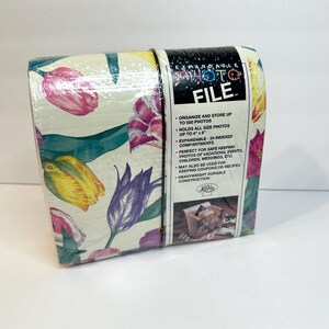 May include: Expandable photo file with a floral tulip design. The photo file is wrapped in plastic and features a cream background with pink, yellow, and purple tulips. The photo file can hold up to 500 photos up to 4" x 6".
